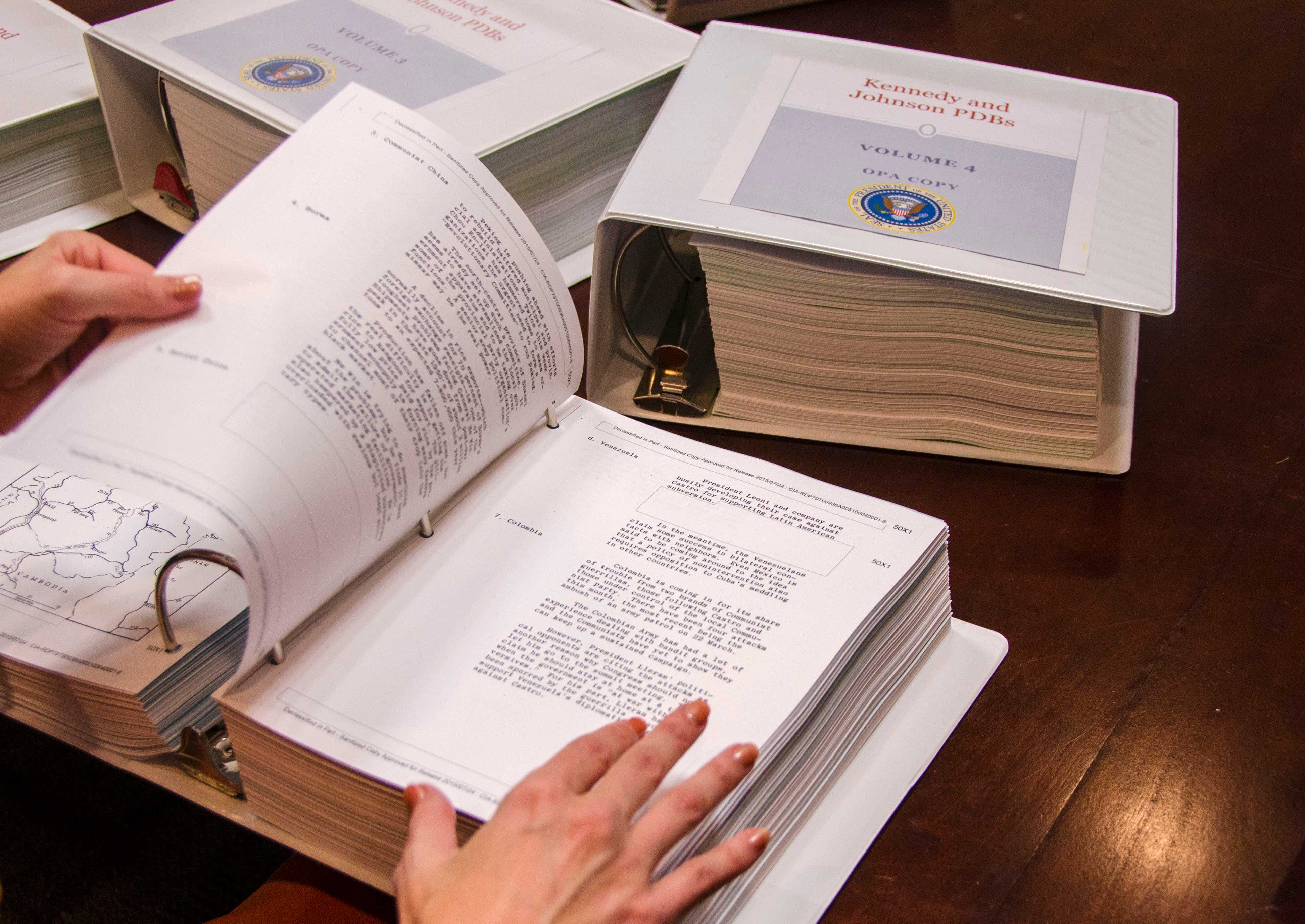 Close-up of hands flipping through large binders of documents with two other binders in the background.