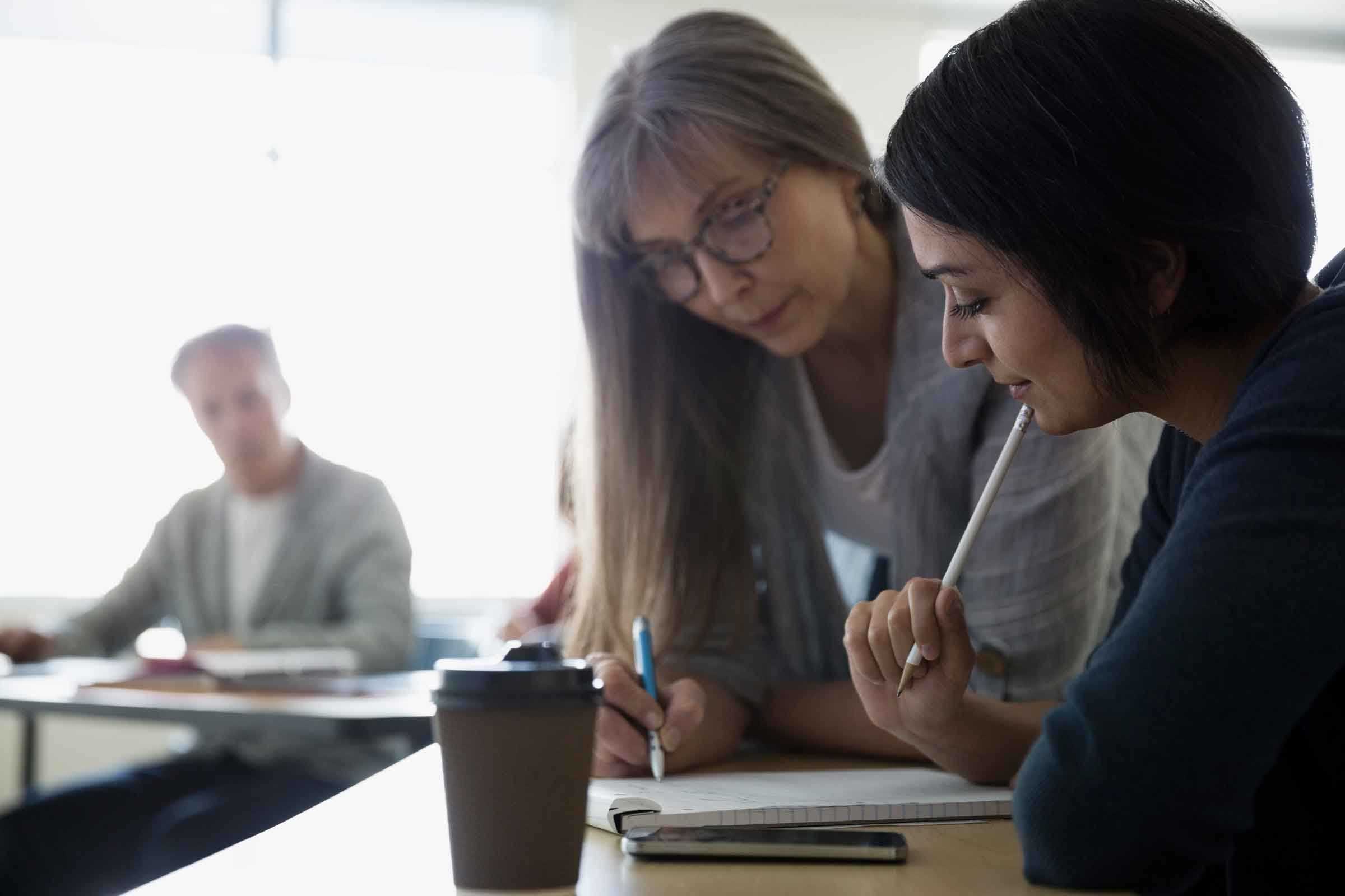 Two women looking at a notepad while holding pencils.