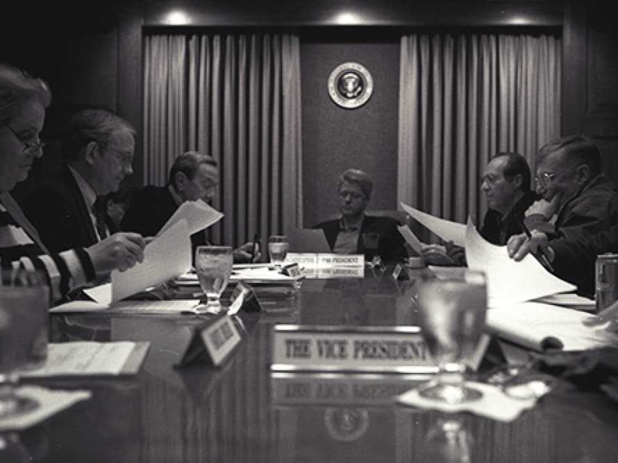 Black and white photo of a group in the boardroom each holding papers.