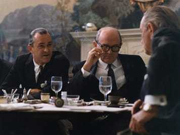 Three men sitting around a table covered in glasses and other items.