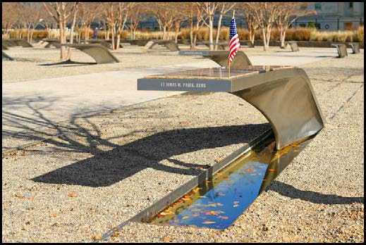 Image of cantilevered bench in the Pentagon's memorial to 9/11 victims. A small US flag is fixed to its corner. The end of the bench, which is above a rectangular pool of water, bears the name Lt. Jonas M. Panik.