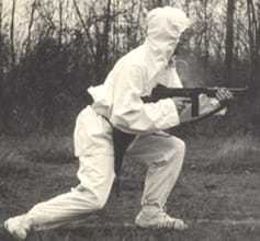 A CIA officer covered head to toe in a white suit, carrying a large gun.