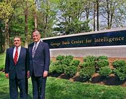Two men in suits posing in front of the George Bush Center for Intelligence.