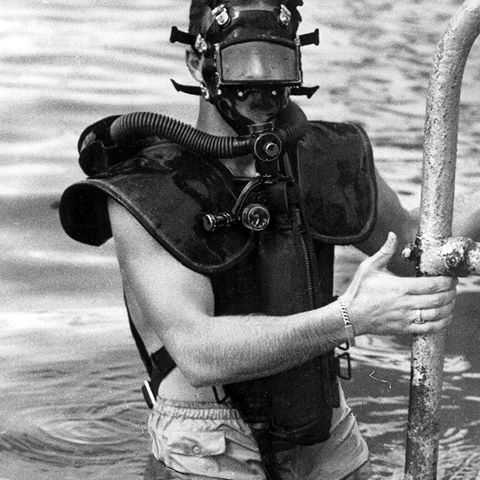 Christian Lambertsen shown using his underwater breathing device climbing out of the water on a ladder.