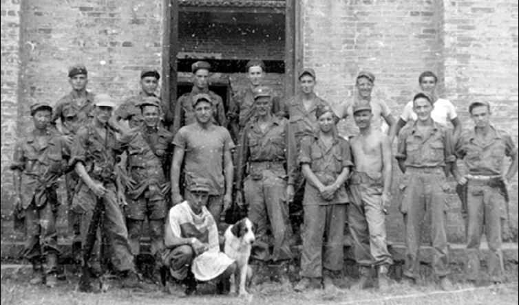 black and white photo of a group of men standing in front of a building, with a dog, during World War II in China.