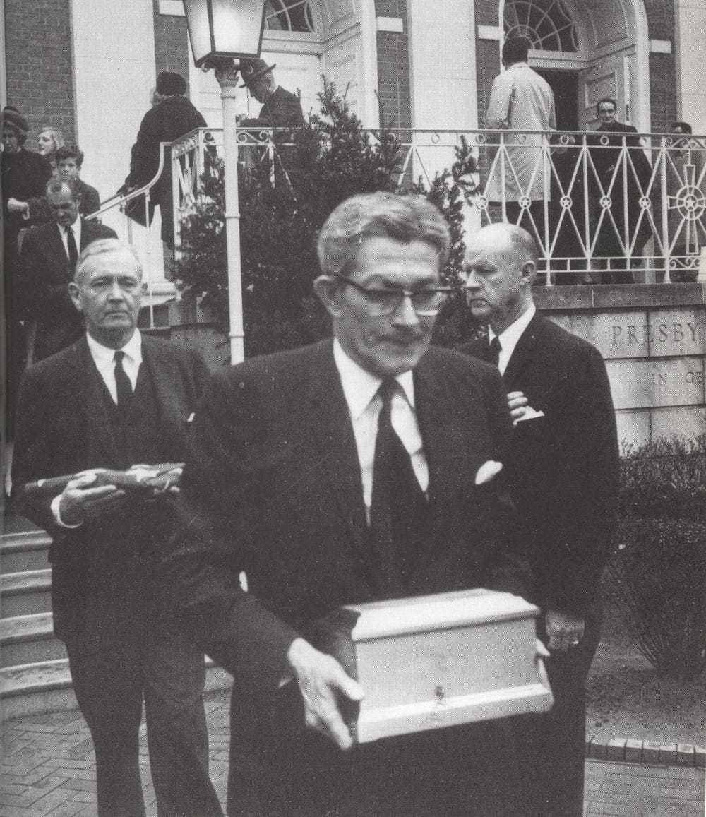 James Angleton holding a box of ashes with two officials standing behind him.