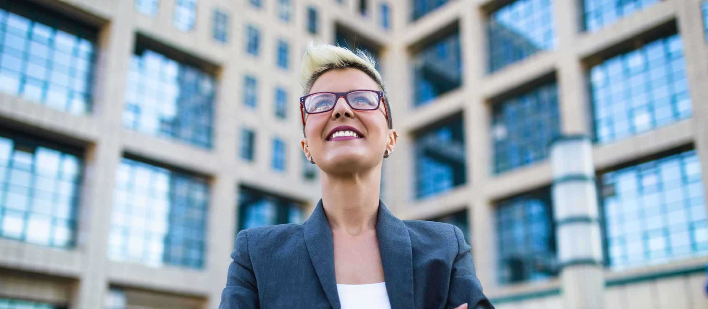 A smiling woman in business wear standing in front of an urban building.