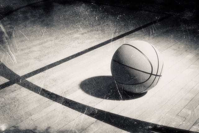 A black and white image of a well-lit basketball on a court, its shadow falling behind it.