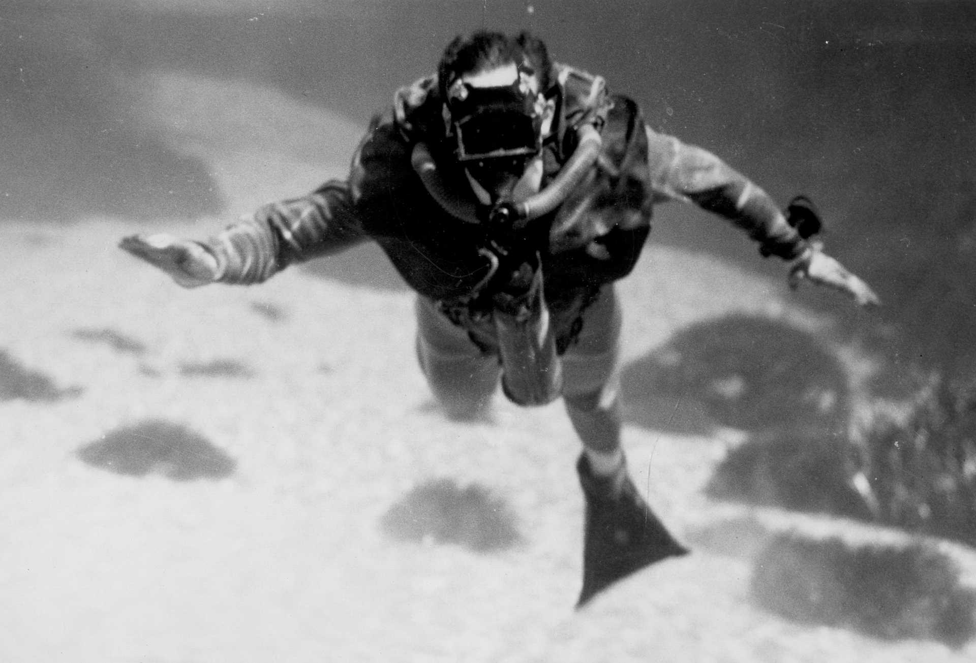 A man swimming underwater using the Lambertsen Amphibious Respirator Unit, an underwater breathing device.