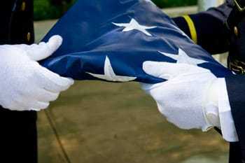 Two gloved hands holding a folded American flag.
