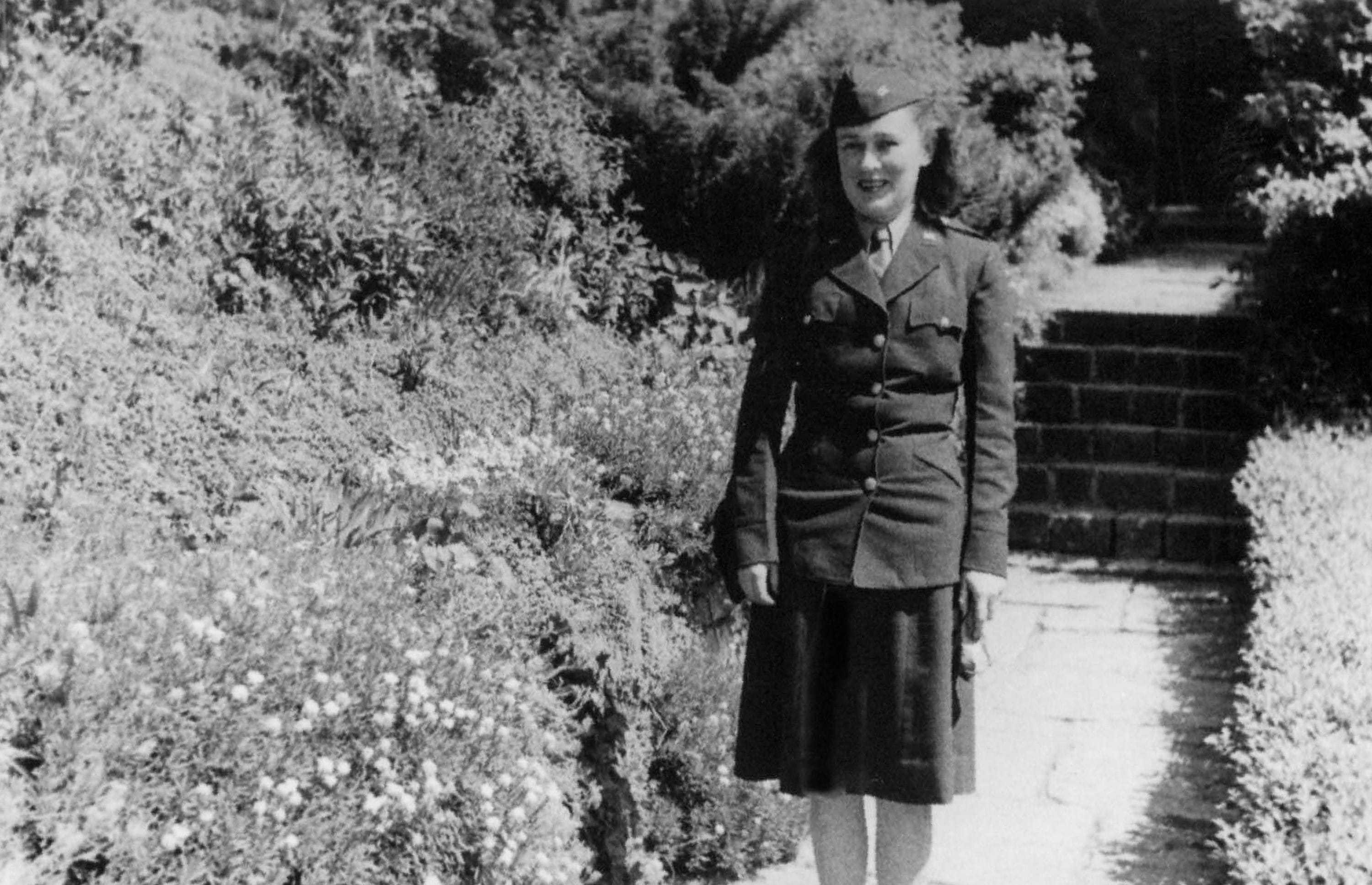 A black and white photograph of Burrell in uniform standing on a path by bushes.