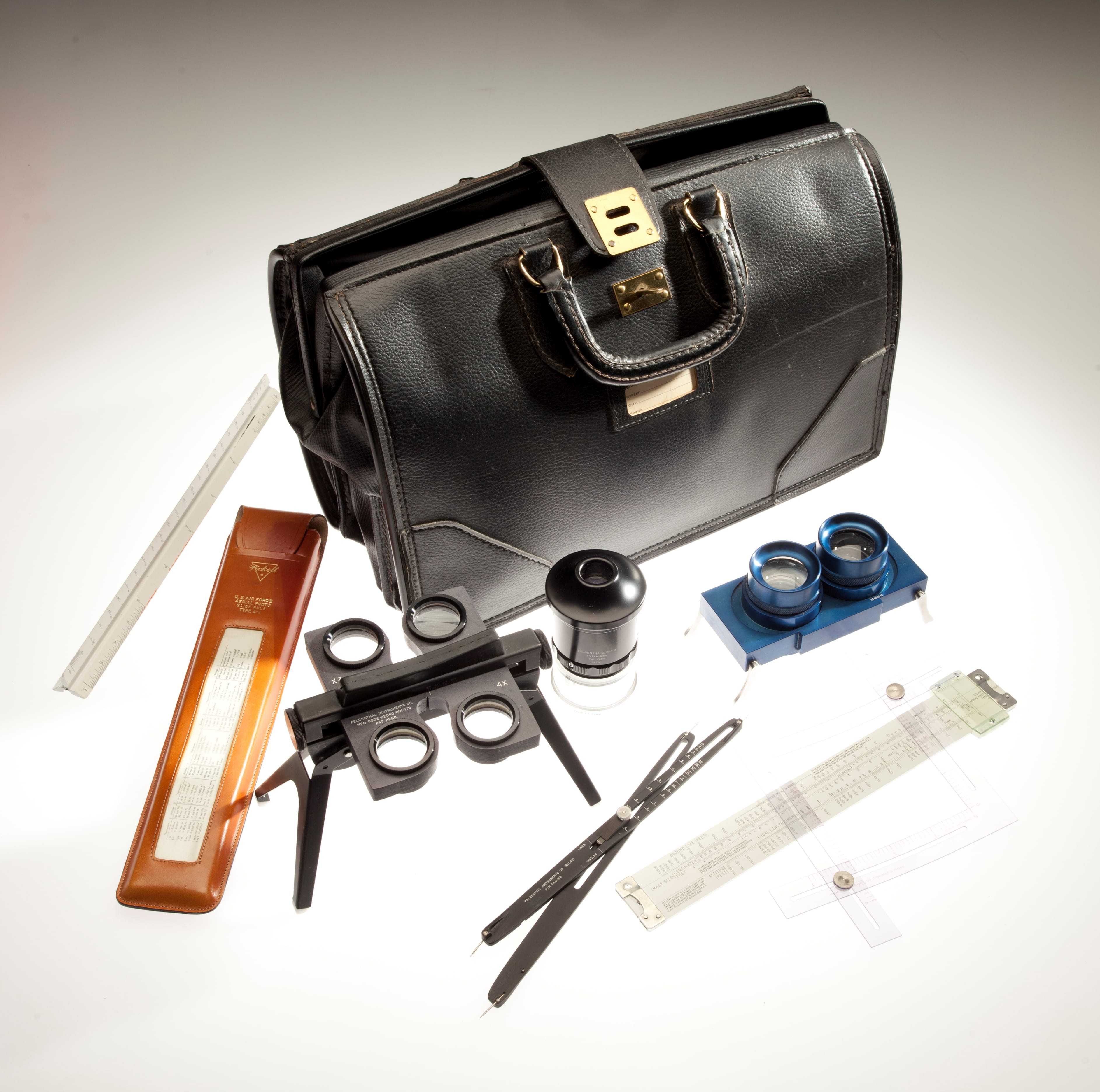 A black briefcase surrounded by magnifying and measuring tools and other items to analyze a photo.