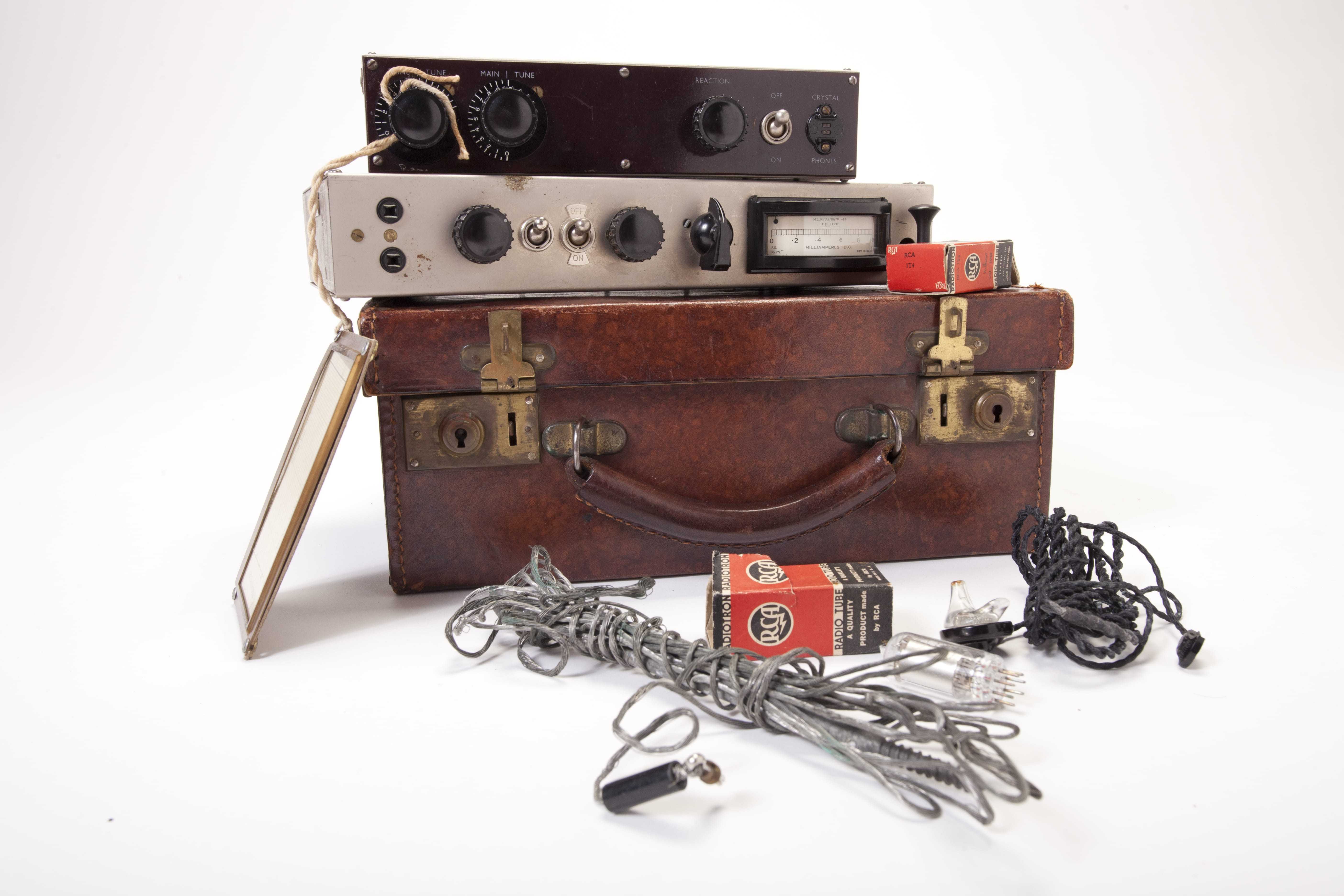 A radio composed of a brown suitcase, transmitter, receiver, frequency card, radium vacuum tube boxes, vacuum tube, and gray and black cords.