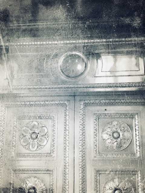 A close up of the top of a sheen elevator with intricate moldings and smoke blurring the image.
