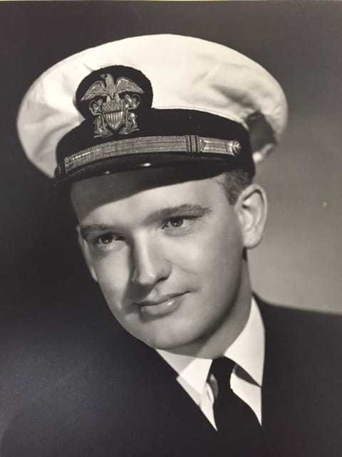 A black and white portrait photograph of a younger James with a Navy cap and suit with a tie.