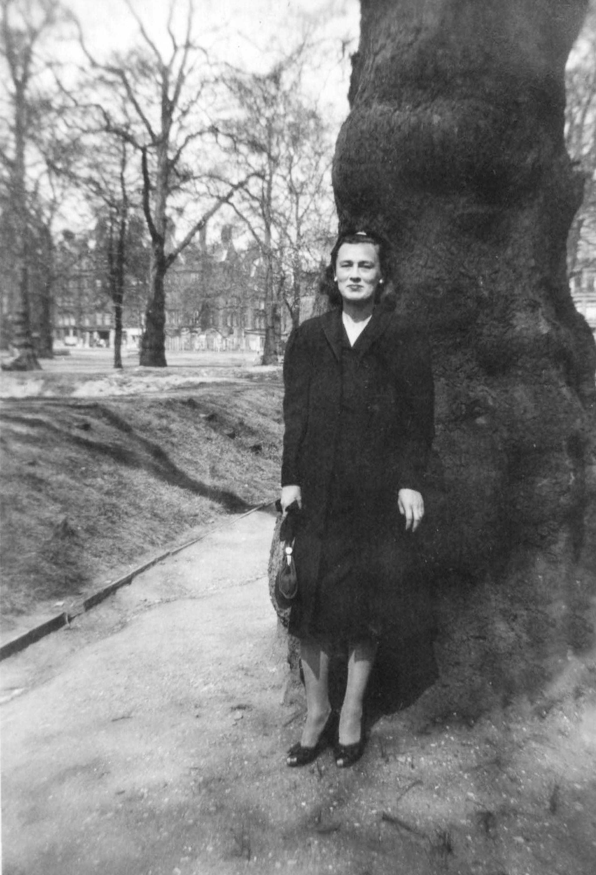 A black and white photograph of Burrell in a dark dress standing in front of a tree in London, 1944.