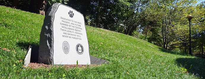 A color photograph of a small tombstone memorial in dedication to the past, present, and future canines of the CIA. A paw is imprinted at the top with the CIA logo below.