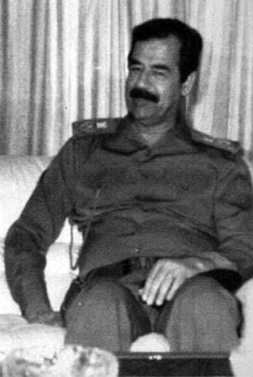 Image of Saddam Hussein sitting on a couch in military garb.
