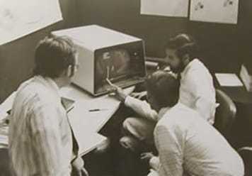 Image of employees gathered around an old computer.