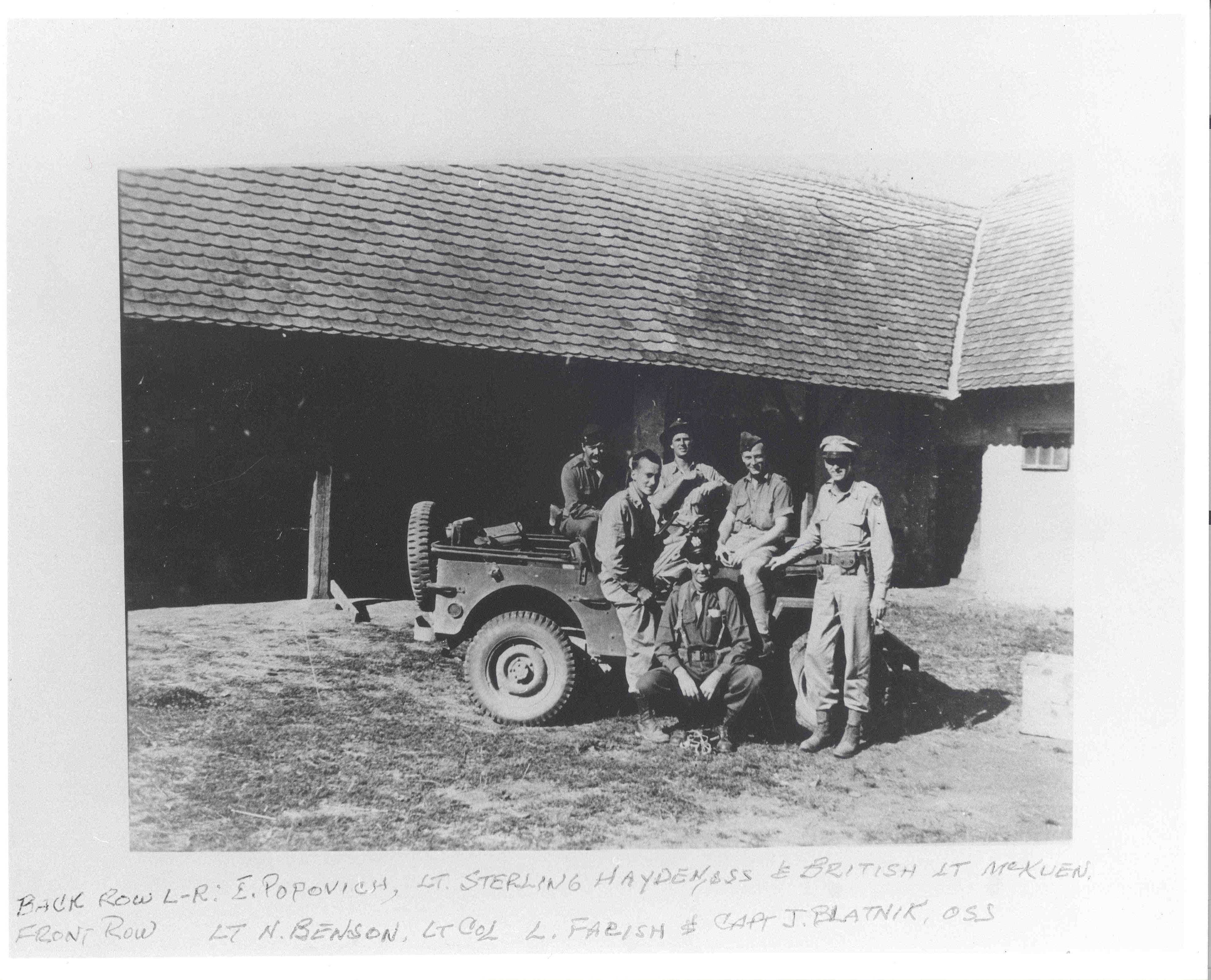 A faded black and white image of a group of men sitting on a car outside of a building.
