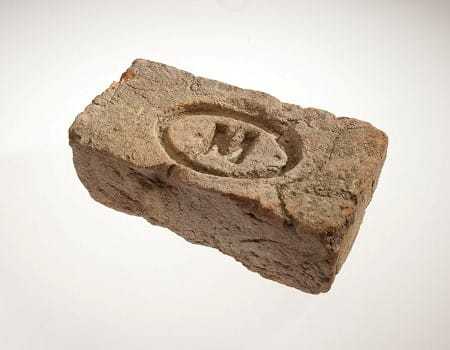 A damaged brick with an engraved oval with an "M" at its center.