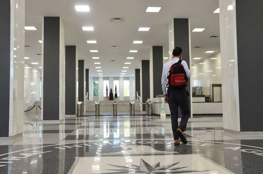 CIA Officer walking down the headquarters hallway with a black and red backpack.