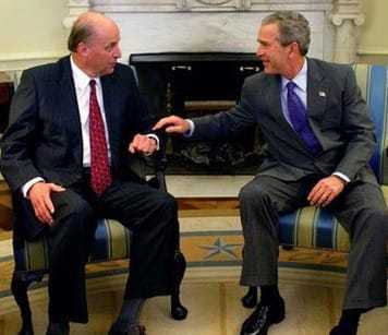 President George W. Bush sitting beside a man patting him on the wrist lauhging.