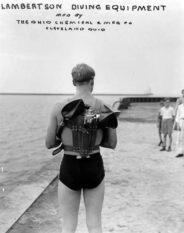 A black and white photograph of a man facing away modeling the Lambertsen diving equipment.