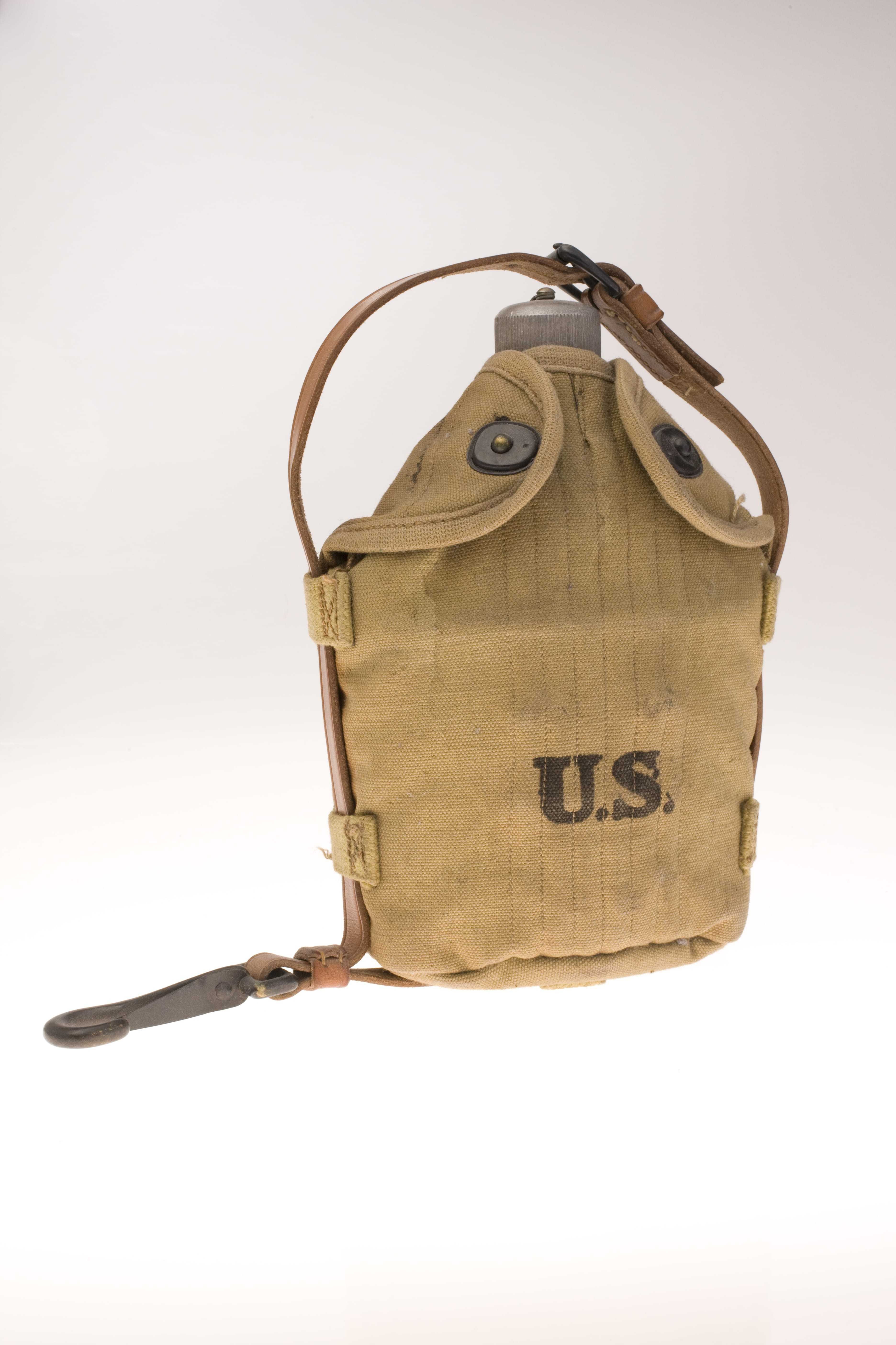 A worn, tan colored canteen with a leather strap and the words "U
