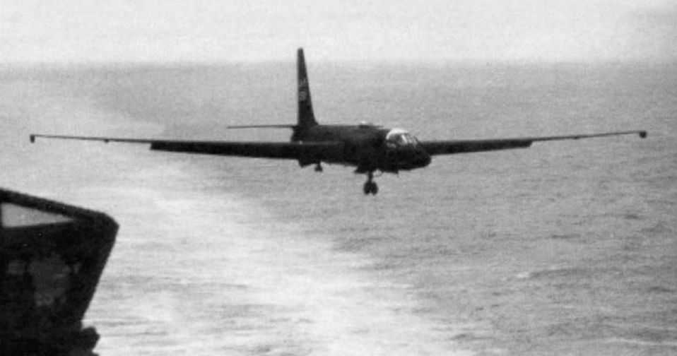 A black and white image of a U-2 aircraft just moments after taking off from a naval ship, with the ocean and the ship in the background.