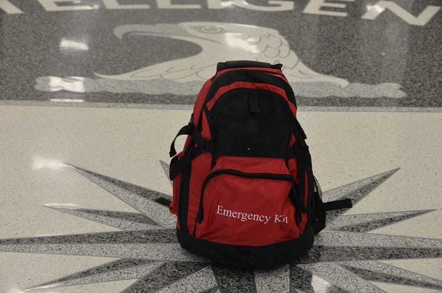 A red and black backpack with the words "Emergency Kit" on it set on the seal.