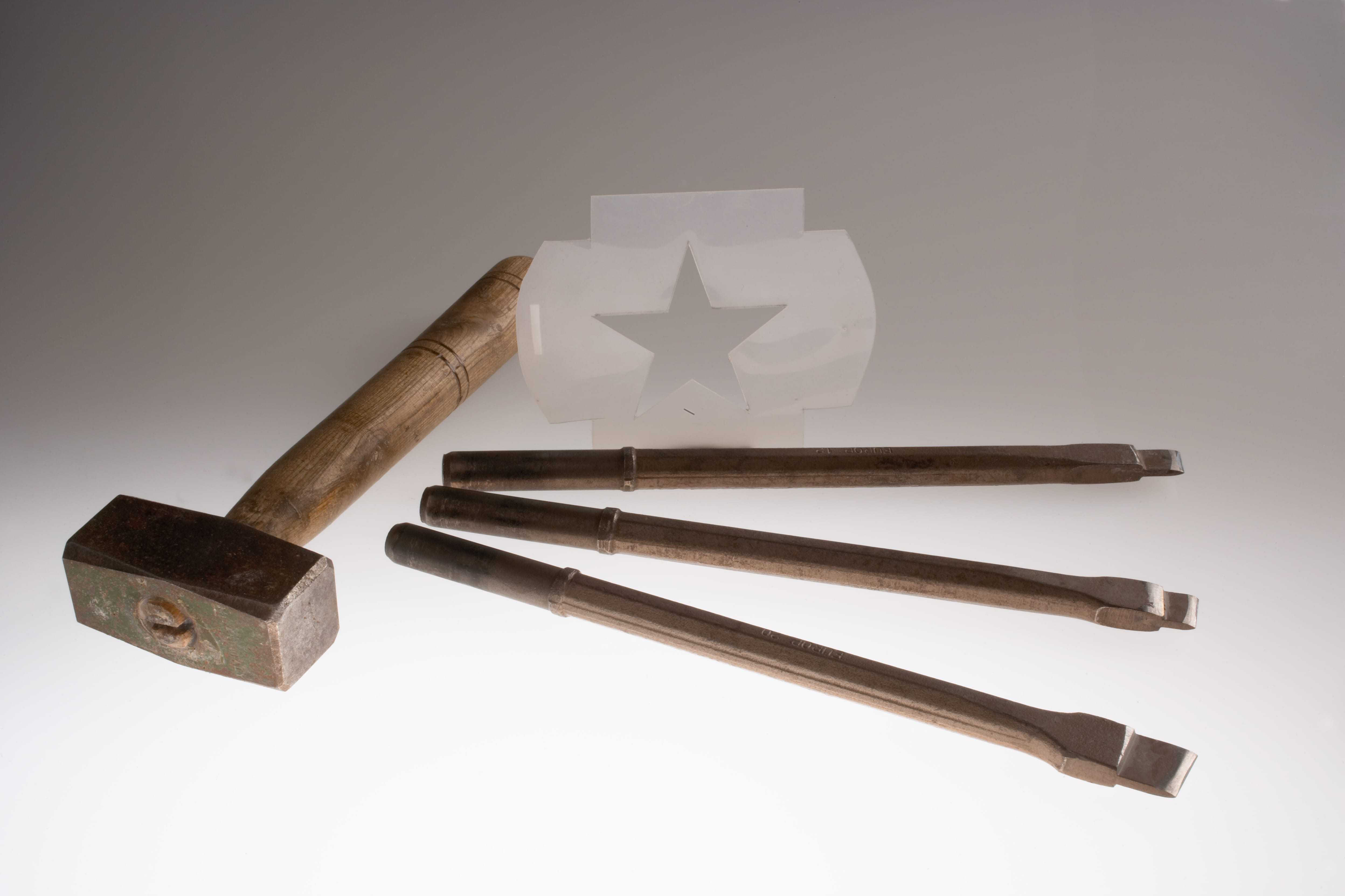 A brown hammer and silver chisels alongside a clear white star template