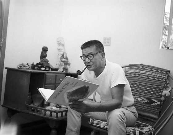 black and white photo of man sitting on chair reading a book