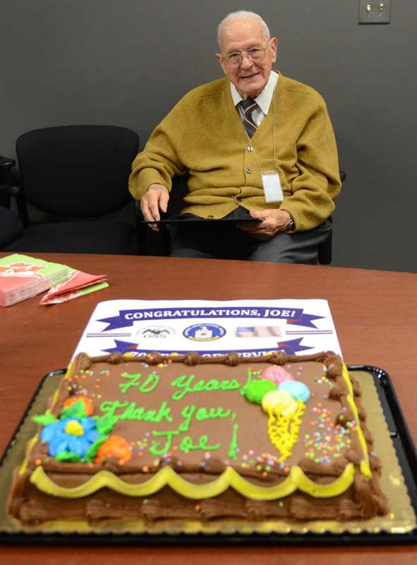 Joe Procaccino with a sign and cake saying, "Congratulations, Joe! 70 Years Thank you, Joe!"