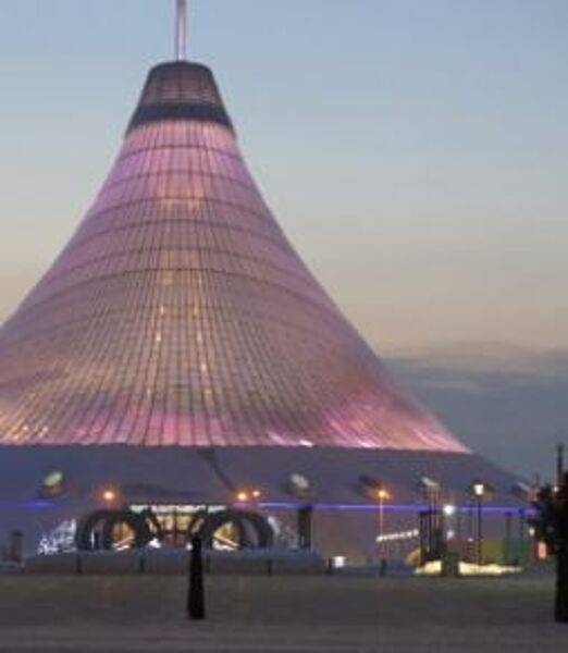 Khan Shatyr (Royal Marquee) is a transparent tent located in the capital city of Nur-Sultan. Designed in a neofuturist style, the architectural project was constructed between 2006 and 2010. The 90 m (300 ft) high tent covers 140,000 sq m (14 ha; 35 acres). Beneath the canopy, which covers an area larger than 10 football stadiums, is an urban-scale park, a shopping and entertainment venue with squares and cobbled streets, a boating river, a shopping center, a mini-golf center, and an indoor beach resort. The transparent material allows sunlight into the area, moderating its temperature year round.
