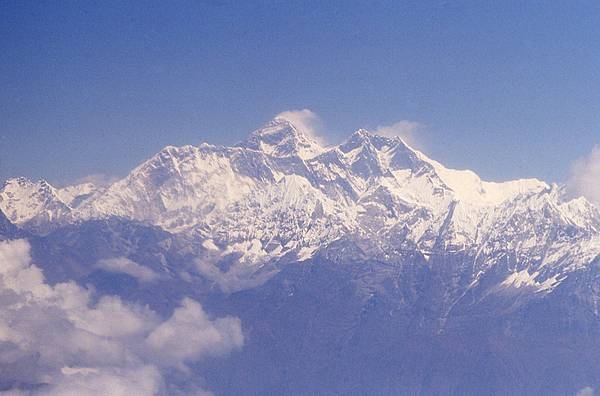 An aerial view of the Himalayas with windswept Mount Everest in the center. The mountain falls on the Nepal-China border and is shared by both countries.
