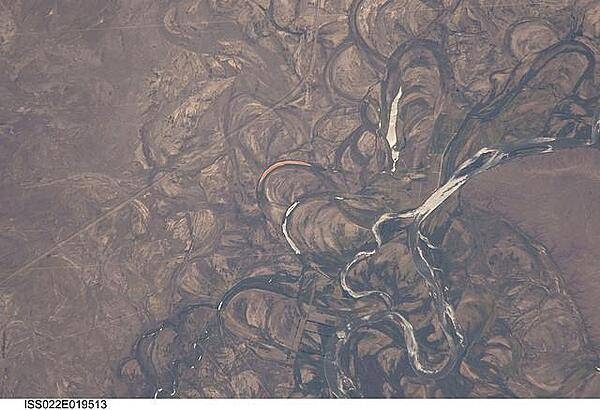 The Rio Negro in Patagonia is recognizable from space as one of the most meandering rivers in South America. This phenomenon is well illustrated in this view, where the entire river floodplain (approximately 10 km (6 mi) wide) is covered with curved relics of channels known as meander scars. The main channel of the river, flowing south at this point 60 km (36 mi) south of the city of Choele Choel (not shown) appears in partial sun glint at right. Sun glint occurs when light is reflected off a water surface directly back towards the viewer, imparting a silvery sheen to those areas. When meander scars contain water they are known as oxbow lakes, some of which are also highlighted by sun glint in the image. Meander scars show the numerous past positions of river bends, produced as the river snaked across the plain in the very recent geological past. The Rio Negro is a dramatic example of how mobile a river can be. The orange tint to the water in one of the oxbow lakes (center) could result from orange salt-loving algae. Image courtesy of NASA.