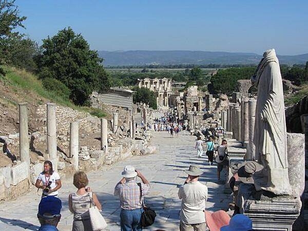 View of the main road in Ephesus, which still bears the marks of chariot wheels. The Library of Celsus may be seen at the foot of the hill. The background is the site of the silted up harbor.