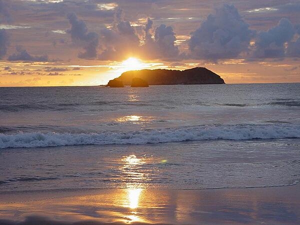 A sunset and its reflection create a golden sheen along a Costa Rican shoreline.