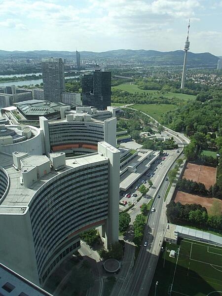 A bird&apos;s-eye view of two of the six Y-shaped UN office buildings in Vienna, Austria, as well as the central cylindrical conference center. In the distance is the 252 m (827 ft) Donauturn (Danube Tower), the tallest structure in Austria.