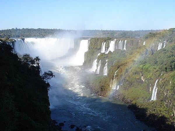 The majestic Iguaçu Falls (Iguazú Falls) on the Brazil-Argentine border. The falls are part of a nearly virgin jungle ecosystem surrounded by national parks on both sides of the cascades. The Iguazú River begins in Parana state of Brazil, then crosses a 1,200-km (750 mi) plateau before reaching a series of faults forming the falls.