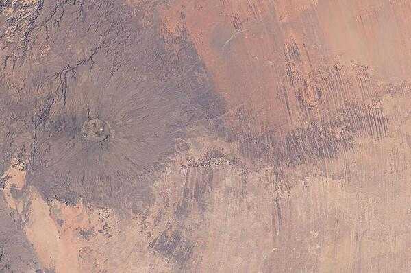 Emi Koussi Volcano and Aorounga Impact Crater in Chad are featured in this striking image photographed from the International Space Station. At left, the broad grey-green shield volcano of Emi Koussi is visible -- its 3,415 m summit is the highest in the Sahara region. The circular Aorounga Impact Crater is located approximately 110 km to the southeast of Emi Koussi and is thought to record a meteor impact approximately 345-370 million years ago. Image courtesy of NASA.