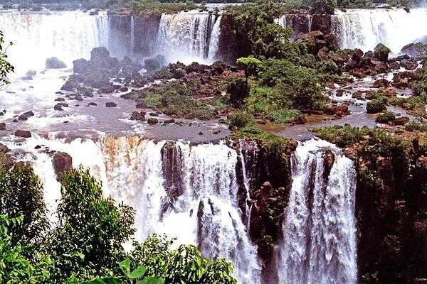 A panoramic view of Iguazu Falls along the Brazil-Argentina border. The falls are shared between Iguazú National Park (Argentina) and Iguaçu National Park (Brazil). The two parks were designated UNESCO World Heritage Sites in 1984 and 1986, respectively. The entire waterfall system consists of some 275 falls that flow over several basaltic layers over an 80 m (262 ft) height and along 2.7 km (1.7 mi) of the Iguazu River.