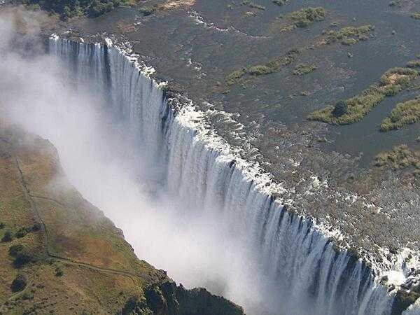 Victoria Falls is located between the borders of Zambia and Zimbabwe. During flood season (February to April), the falls form the greatest sheet of falling water on earth. Victoria Falls is 1.7 km (1.1 mi) wide and 108 m (360 ft) high and is known locally as Mosi-oa-Tunya (The Smoke that Thunders).  
View of Victoria Falls on the Zambezi River as seen from the Zambian (eastern) side.