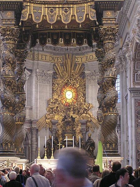 A view of the baldachin, a massive pavilion-like structure (30 m or 98 ft tall) that stands beneath the dome of St. Peter's Basilica in Vatican City. Viewed through the structure are the Cathedra Petri (Throne of St. Peter) and the Gloria, a stained glass sculpture, both by Bernini.