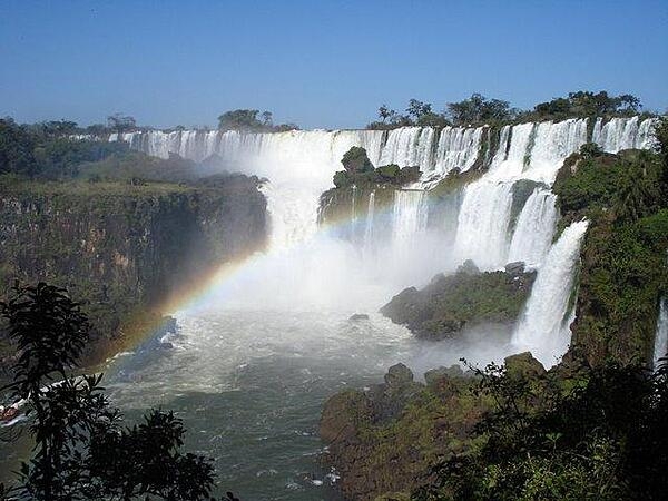 A rainbow appears in the mist of Iguazu Falls. The falls are part of a nearly virgin jungle ecosystem surrounded by national parks on both the Argentine and the Brazilian sides of the cascades. The Iguazu River begins in Brazil's Parana state, then crosses a 1,200-km (750 mi) plateau before reaching a series of faults that form the falls.