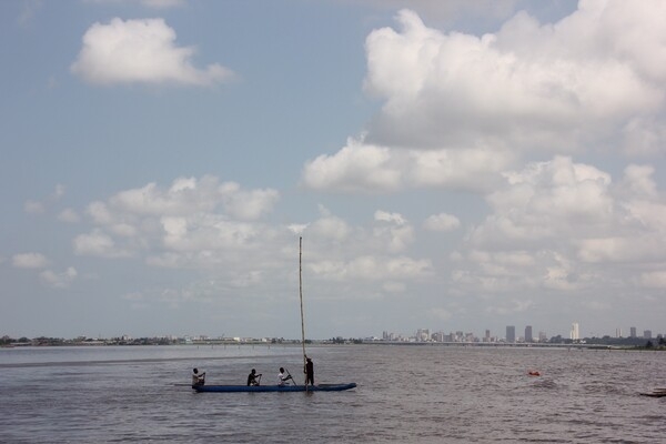 Fishermen ply their trade in Abidjan, Côte d'Ivoire; the city skyline appears in the background.