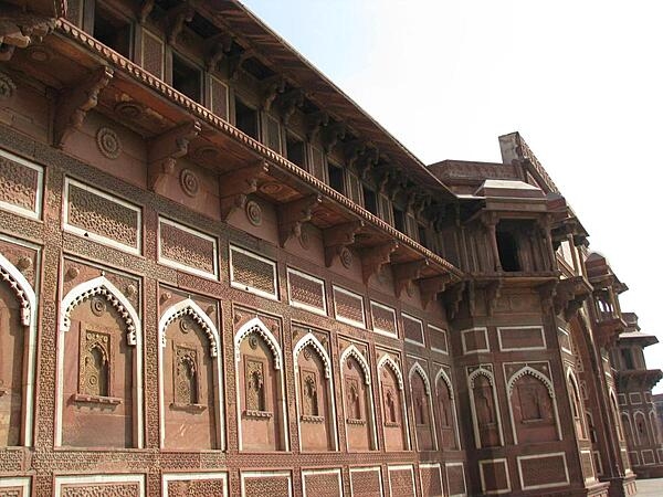 India's Agra Fort, also known as the Red Fort of Agra, represents the opulence and power of the Mughal Empire in the 16th to the early 18th century. The fortress, located on the right bank of the Yamuna River, is built of red sandstone and covers a length of 2.5 km (1.6 mi). It is surrounded by a moat, which encloses several palaces, towers, and mosques.  Shown here is the Jahangiri Mahal, the most prominent building at Agra Fort.