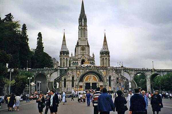 Pilgrims and visitors in Lourdes, France. The Rosary Basilica in the foreground serves as an entrance to the larger Basilica of the Immaculate Conception. Lourdes is the reputed site of 18 apparitions of the Virgin Mary in 1858. The town is one of the world's greatest pilgrimage sites, hosting some 5 million visitors annually.