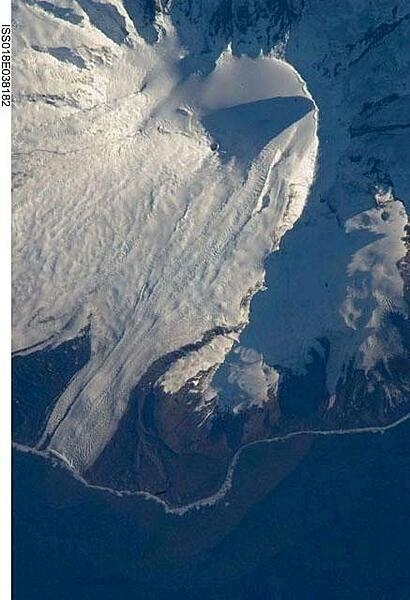 The northeastern slopes of Big Ben volcano on Heard Island are visible in shadow at the top right of this photo. Mawson Peak (small circle in the upper center of the image), sits in a breached caldera (collapsed and empty magma chamber beneath a volcano) on the southwestern side of the volcano -- the peak's shadow points to the crescent-shaped caldera rim. This image, taken during the Southern Hemisphere summer, also shows the dark brown volcanic rock that forms the island. The southwest-pointing tongue of ice is Gotley Glacier. Image credit: NASA.